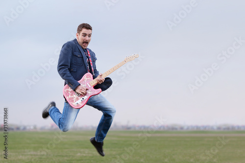 Guitar hipster guy jumping and playing funky rock music outdoors