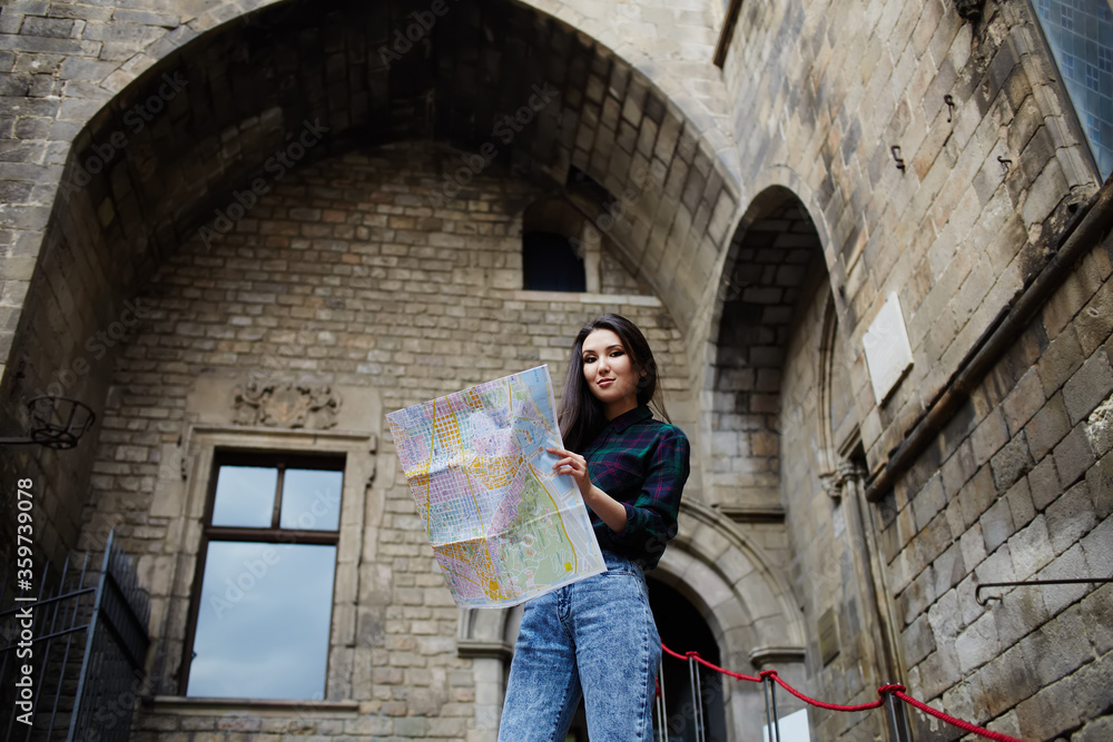 Charming tourist girl holding city map in the hands smiling, beautiful girl studying city map standing in gothic quarter in Barcelona, young tourist woman on vacation with a map in gothic quarter