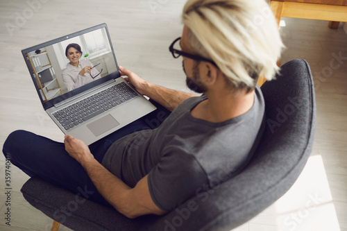 Canvas Print Young guy speaking with online doctor on laptop at home