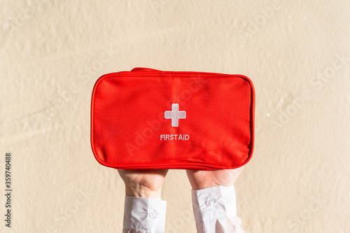 . First aid kit red bag in woman hand on the sand beach. Travel, flat lay, lifestyle.