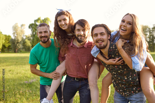 Group of happy friends piggyback ride laughing hugging on nature in summer in spring.