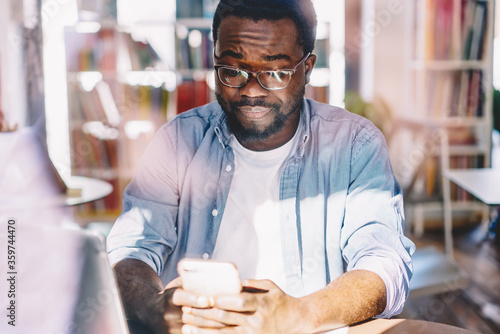 Canvas Print Sad ethnic man interacting with smartphone in light modern office