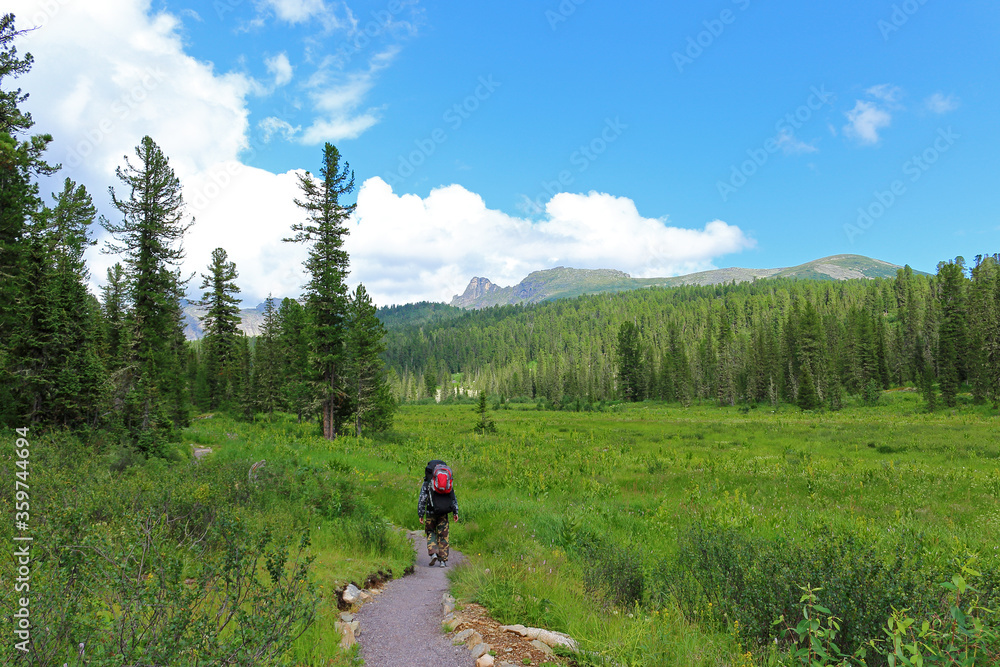 Man with a heavy backpacks hiking on a trail in the mountains landscape. Active healthy lifestyle and adventure vacations in Nature Park Ergaki, Russia, Siberia. Traveling alone into the wild nature