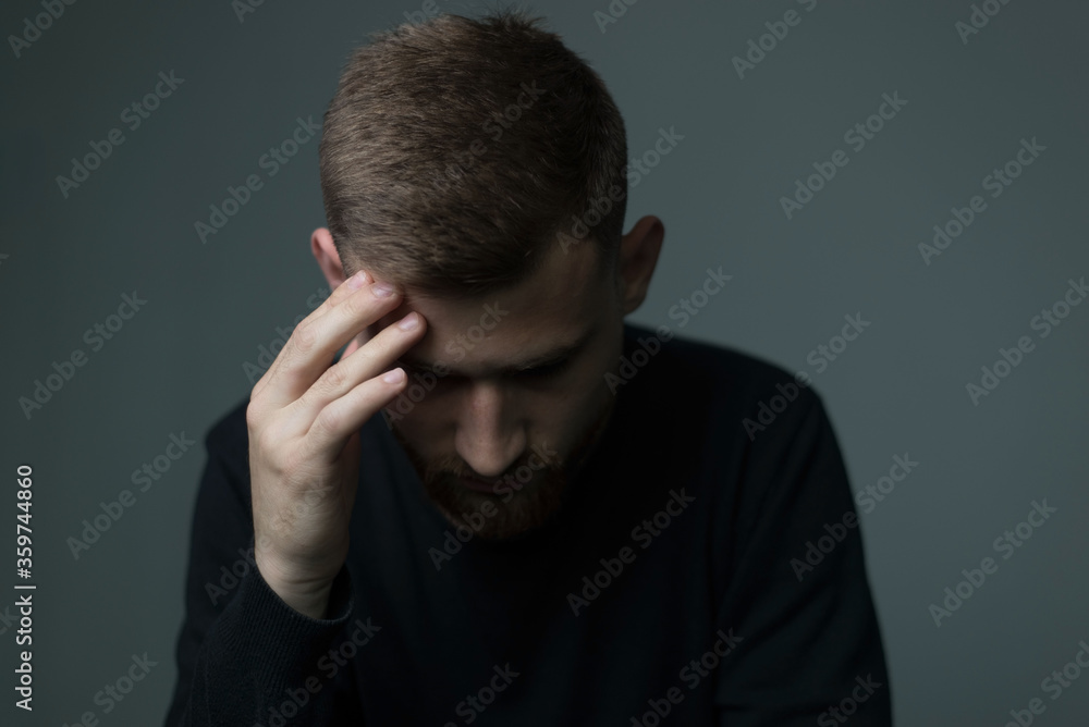 Portrait of a bearded young man of twenty-five, in black, holds his hand to his head, suffers from a headache. On a gray background Portrait of a bearded young man of twenty-five, in black, holds his hand to his head, suffers from a headache. On a gray background