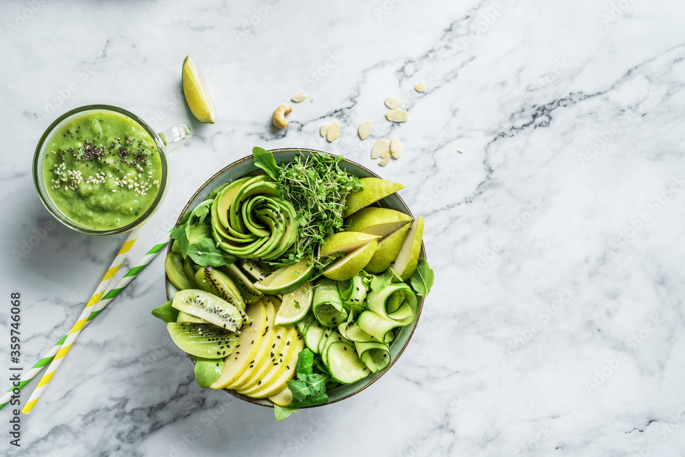 Obraz premium Fresh summer salad with avocado, kiwi, apple, cucumber, pear, micro greens, lime and sesame on light marble background with smoothie. Healthy food, clean eating, Buddha bowl salad, top view