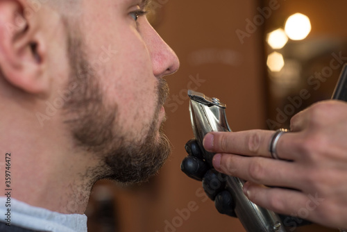 a hairdresser cuts a bearded young guy with a hair trimmer, combing the hair on his head. Work of the master in men's haircut in a barbershop. photo