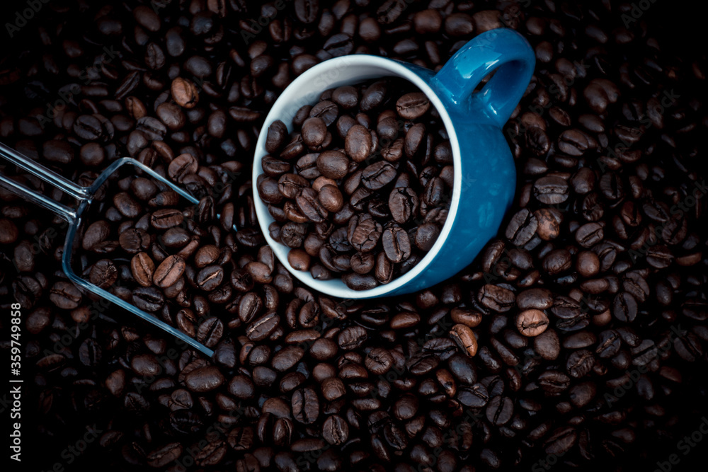 Fototapeta premium blue coffee cup filled with black coffee beans and surrounded by them