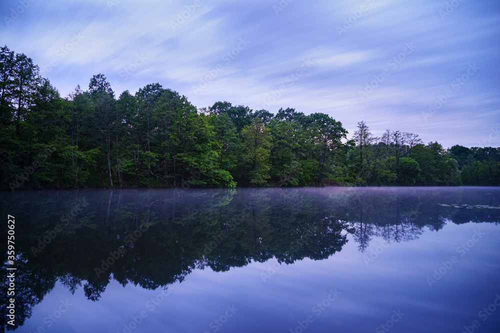 Early foggy morning on the lake. Long exposure nature photography. Calm water and forest with reflection. Early foggy morning on the lake. Long exposure nature photography. Calm water and forest with reflection.