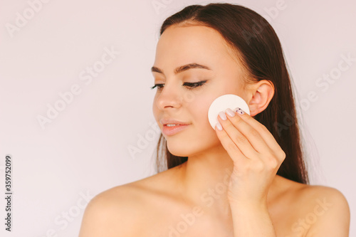Portrait young sensual woman with perfect smooth skin remove make up on face with cotton pads isolated white background. Beautiful happy girl clean face from cosmetics. Cleansing lotion, skin care