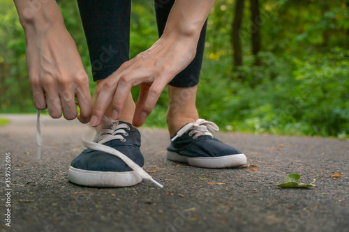 Close-up of women s hands tying shoelaces in dark blue sneakers on a jog in the woods.