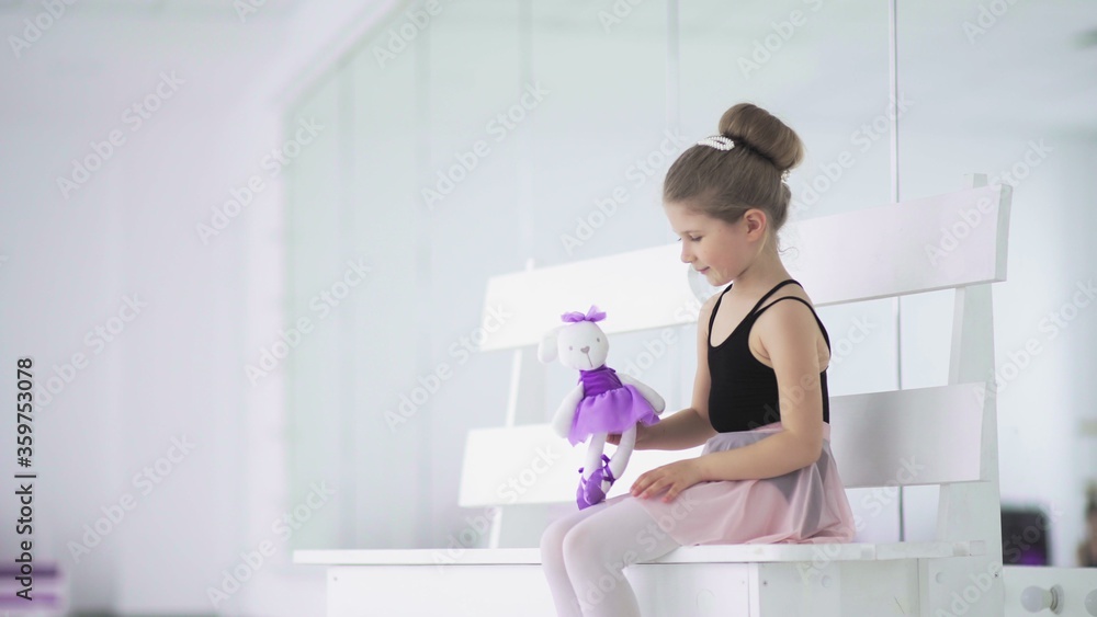 Little girl with toy in hand are sitting on bench in ballet classroom Little girl with toy in hand are sitting on bench in ballet classroom