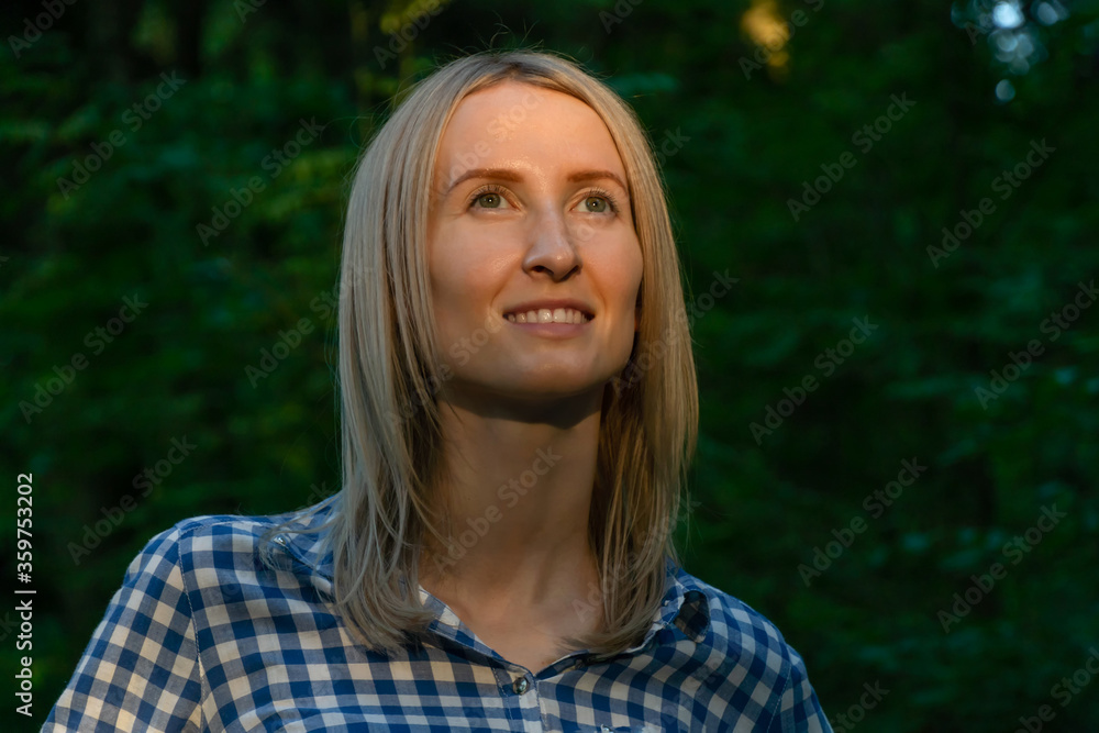 Portrait of a young blonde woman in the forest on which the rays of the sun fall
