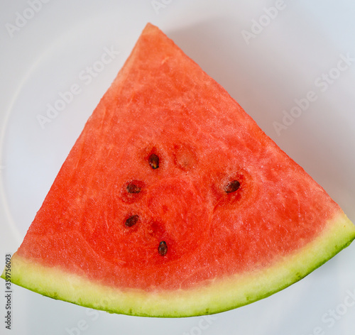 Red watermelon slice with green peel and black seeds, white background.
