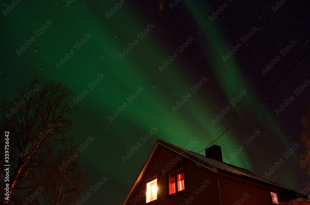 strong aurora borealis dancing on winter night sky over small house in northern Norway strong aurora borealis dancing on winter night sky over small house in northern Norway