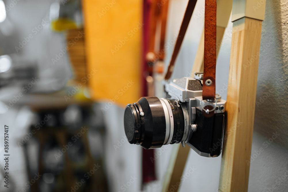 retro film camera hangs on a strap against a white wall and a yellow warm lamp. Horizontal retro film camera hangs on a strap against a white wall and a yellow warm lamp. Horizontal