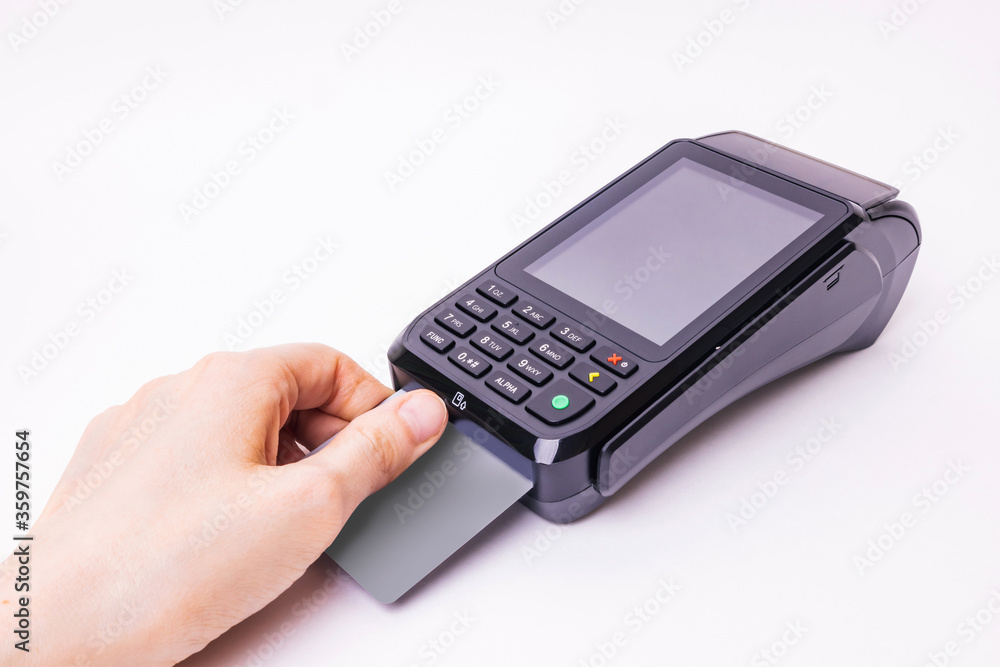 A hand inserts a plastic payment card into the terminal. Banking equipment. Acquiring. Acceptance of bank credit cards. Pos terminal, light background. A hand inserts a plastic payment card into the terminal. Banking equipment. Acquiring. Acceptance of bank credit cards. Pos terminal, light background.