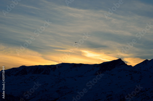 paraglider on a beautiful dawn sky with majestic snow covered mountain underneath in the arctic circle
