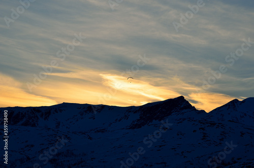 paraglider on a beautiful dawn sky with majestic snow covered mountain underneath in the arctic circle