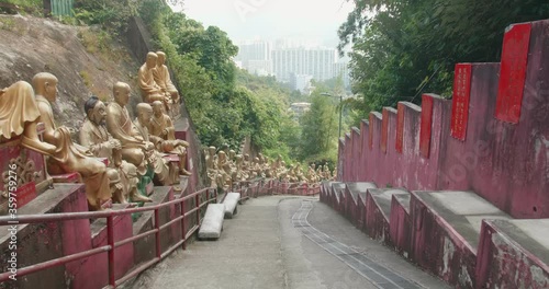 Tracking in (TIN) of buddha statues in rows. Ten Thousand Buddhas Monastery's main alley going down, Sha Tin, Hong Kong. Peaceful golden religious sculptures. High dynamic range footage. photo