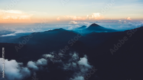 Aerial photo from airplane cockpit of a sky with white puffy clouds with sunset lights over mountains silhouette in evening time. Fascinating nature beauty over land. Perfect background for website