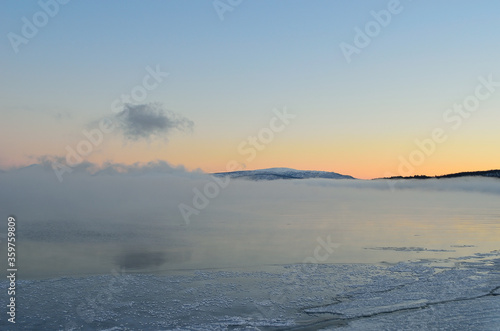 pink sunset sky in winter over frozen fjord and dense ice fog