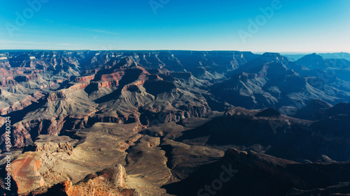 Aerial view of Grand Canyon National Park with antique Colorado Plateau geological rocks and cliffs over abysses, bird's eye view of beautiful scenery in famous touristic sight viewpoint with blue sky