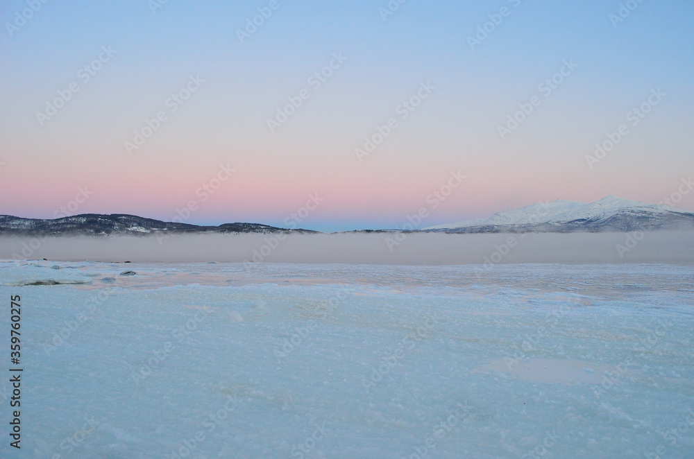 Obraz premium pink sunset sky in winter over frozen fjord and dense ice fog