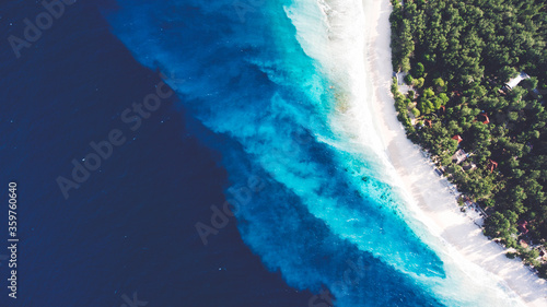 Top view aerial drone photo of stunning colored sea beach with crystalline water. incredibly beautiful blue ocean meet with powder-white seashore surrounded by tropical rainforest or palm trees jungle