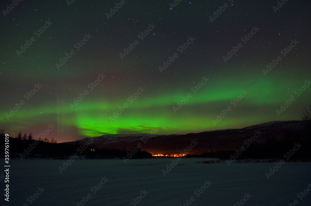 magnificent aurora borealis over frozen river bed and snowy mountain in the cold arctic circle night