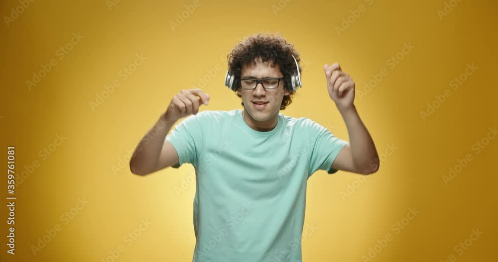 Close up shot of happy asian guy with curly hair putting on headphones and dancing, isolated on yellow background - leisure, fun concept 4k slow motion Close up shot of happy asian guy with curly hair putting on headphones and dancing, isolated on yellow background - leisure, fun concept 4k slow motion