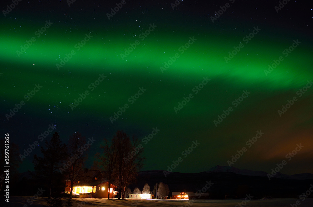 green strong aurora borealis over field and homes in the arctic circle winter landscape