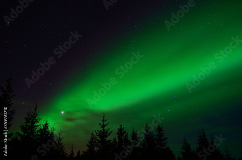 solar flare creates strong vibrant aurora borealis on the winter night sky over forest and trees © Arcticphotoworks