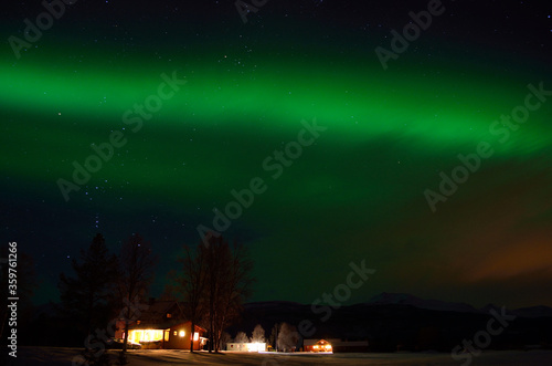 green strong aurora borealis over field and homes in the arctic circle winter landscape