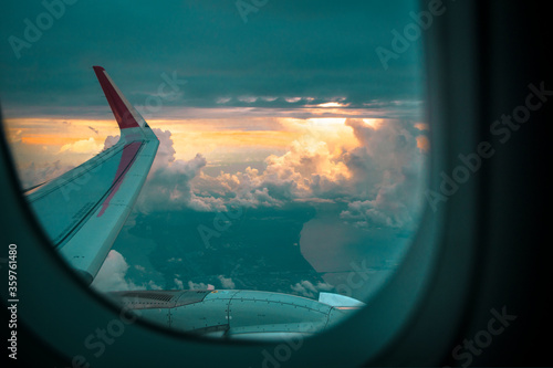 Photo of beautiful golden sunset and withe clouds at high altitude from an airplane window showing the airplane wing and engine