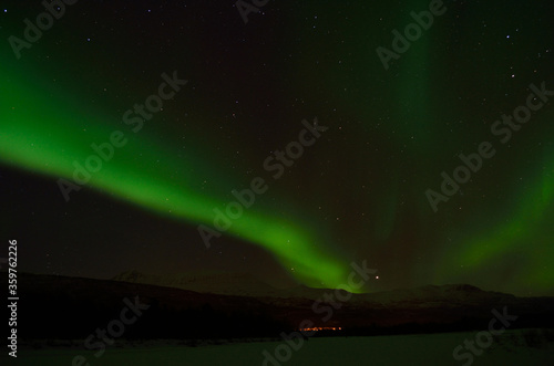 Fantastic vibrant and strong aurora borealis, northern light over snow covered mountain and frozen river bed in the arctic circle at night