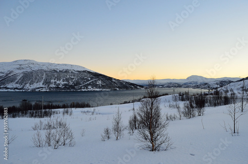 Beautiful snowy winter landscape with vibrant colourful dawn sky, majestic mountains and cold fjord water