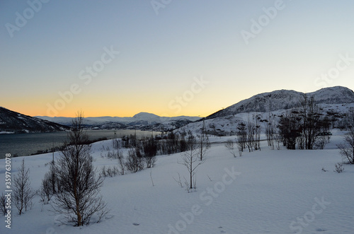 Beautiful snowy winter landscape with vibrant colourful dawn sky, majestic mountains and cold fjord water