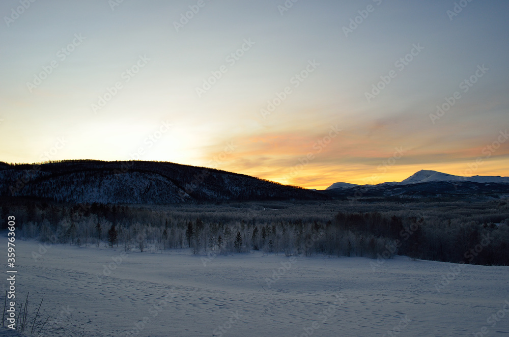 Scenic snowy mountain with vibrant colourful sky and white frost covered forest in the front Scenic snowy mountain with vibrant colourful sky and white frost covered forest in the front