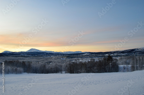 Scenic snowy mountain with vibrant colourful sky and white frost covered forest in the front © Arcticphotoworks