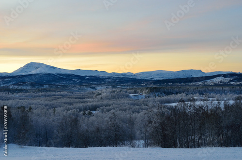 Scenic snowy mountain with vibrant colourful sky and white frost covered forest in the front