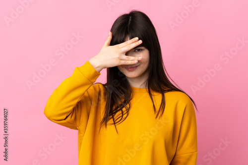 Young Ukrainian woman isolated on pink background covering eyes by hands and smiling