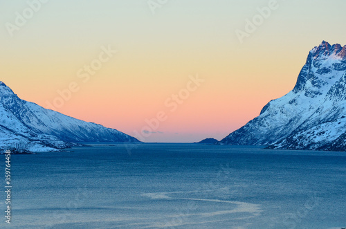 Colourful dawn sky over arctic fjord surrounded by snowy majestic mountains