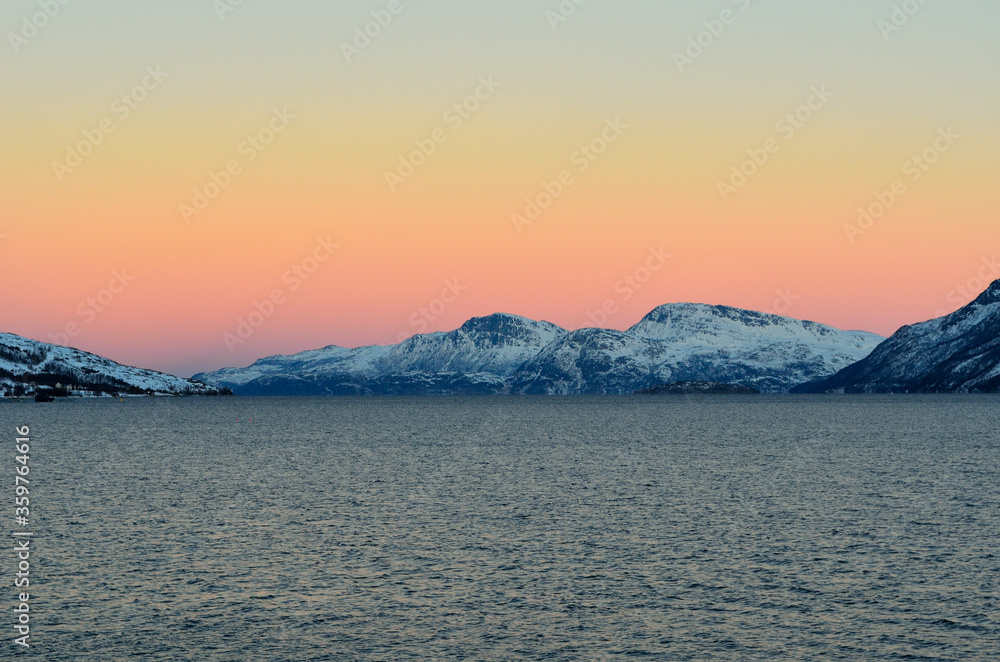 Vibrant colours on dawn sky over cold arctic fjord water and majestic snowy mountain range
