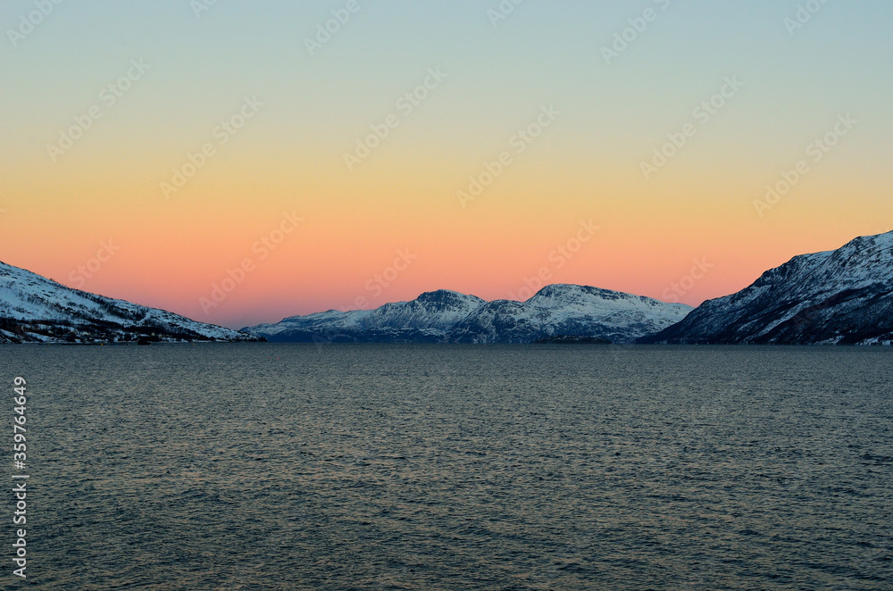 Vibrant colours on dawn sky over cold arctic fjord water and majestic snowy mountain range