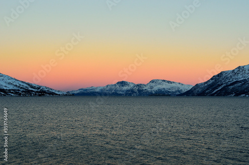 Vibrant colours on dawn sky over cold arctic fjord water and majestic snowy mountain range