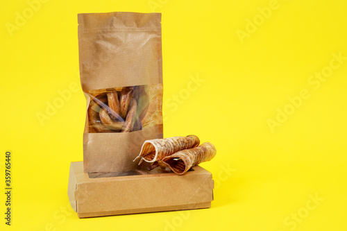 craft box and package with transparent top with tasty dried snacks for pets inside on yellow background, close up, copy space for advertising text. Pet care. Pet supplies.