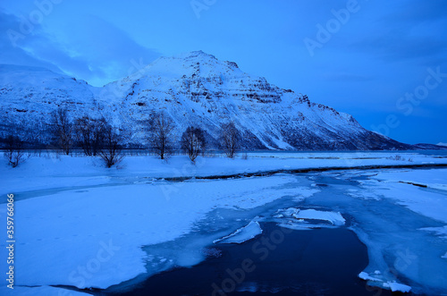 frozen river stream  snowt field and mighty mountain during the winter blue hour in northern Norway