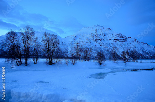 frozen river stream, snowt field and mighty mountain during the winter blue hour in northern Norway