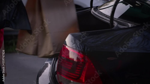 Beautiful girl is putting shopping bags into car trunk and smiling. loading shopping into boot of car. Eco paper bags with groceries from the supermarket. Outdoor. Close-up. photo