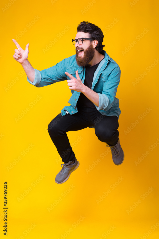 Excited bearded man is jumping high showing cool gesture over yellow background